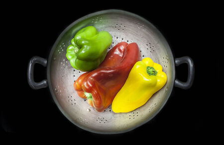 Colander with three different capsicums isolated on a black backgroundの写真素材