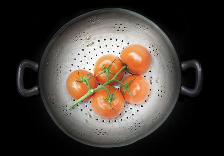 Colander with five tomatoes isolated on a black backgroundの写真素材
