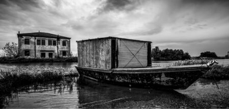 Black and white image of an old boat on a river and an old buildingの写真素材
