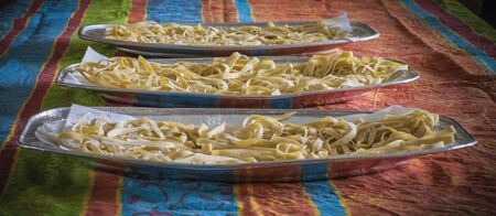 Three trays with homemade pasta on a table with clothの写真素材