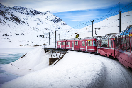 Bernina Express train, one of the highest railway in the world, goes across a little bridge in snowy mountain near a frozen lakeのeditorial素材