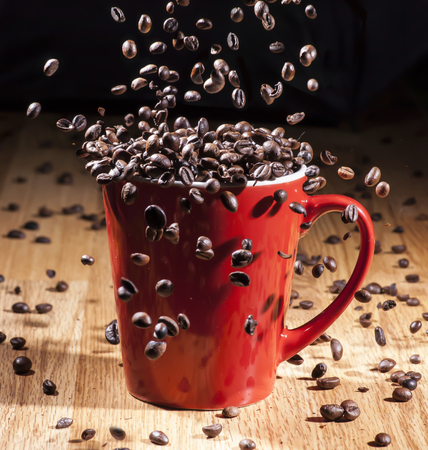 Espresso big red cup on a wooden table with coffee beans falling insideの写真素材