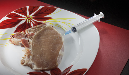 Concept genetically modified organism: syringe and raw meat on a dishの写真素材