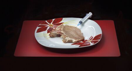 Concept genetically modified organism: syringe and raw meat on a dish isolated on a black backgroundの写真素材