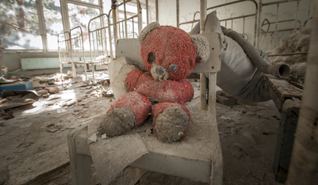 Old red teddy bear sitting on a chair in an abandoned kindergarten in Pripyat - Chernobyl nuclear power plant zone of alienationの写真素材