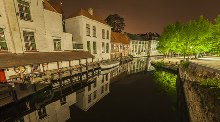 Romantic nocturnal view of a canal in Bruges. Buildings, trees and boats are reflected in the waterの写真素材