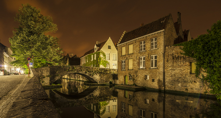 Romantic nocturnal view of a canal in Bruges. Buildings, trees and the bridge are reflected in the waterの写真素材