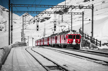 Bernina Express train, one of the highest railway in the world, goes across a little bridge in snowy mountain near a frozen lakeのeditorial素材