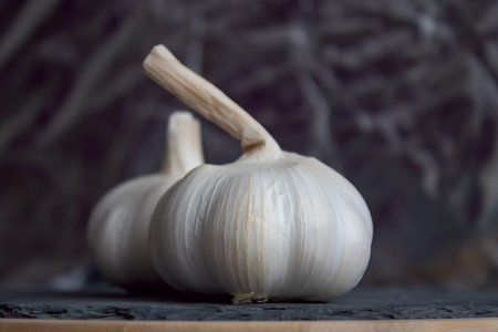 Two bulbs of garlic lie on a stone cutting board. close-up. daytime lighting. Blurred background. Place for text. copy-paste.の写真素材