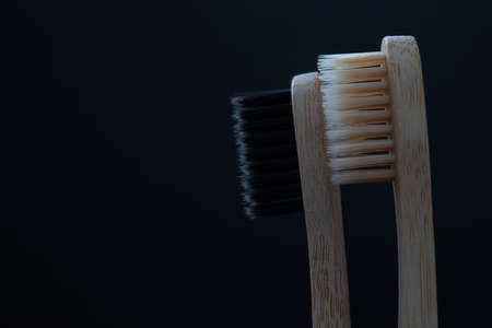 Two bamboo toothbrushes with black and white bristles. Black background. Place for text. copy-paste. The concept of caring for teeth and gums. Prevention of dental disease.の写真素材