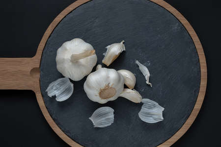 Two bulbs of garlic lie on a kitchen cutting board. close-up. daytime lighting. view from above. Place for text. copy-paste.の写真素材