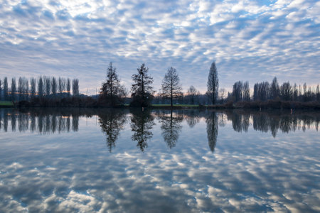 Winter sunset on the shore of a lake with clouds reflected in the waterの写真素材