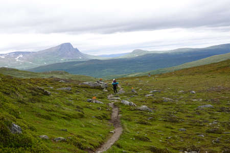 Person walking on a hiking trail in a green valley in summer with some cloudsの写真素材