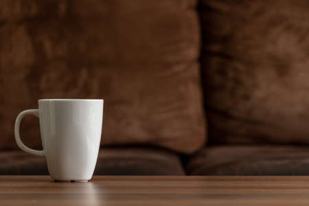White mug on a wooden table with a brown couch background. copy space left over for text and imagesの写真素材