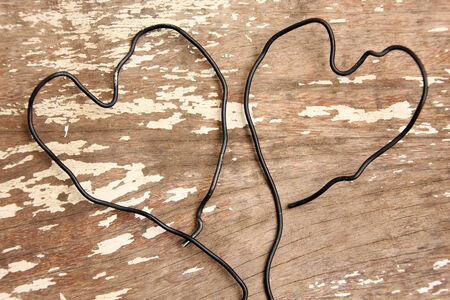 wire bent in shape of two heart togather on wooden backgroundの写真素材