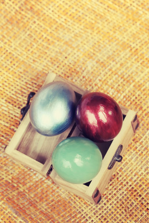 Colorful easter eggs in small wood case on bamboo weave sheet background. Process in vintage style.の写真素材