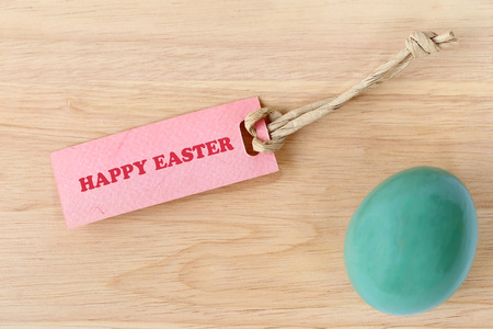 Happy Easter text on paper tag with an easter egg on wood background.