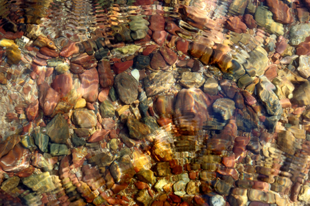 Blurred colored pebbles on the beach with water texture, abstract background.の写真素材