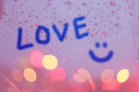 Rain drops and the word love write on window with light bokeh, rainy season abstract background.の写真素材