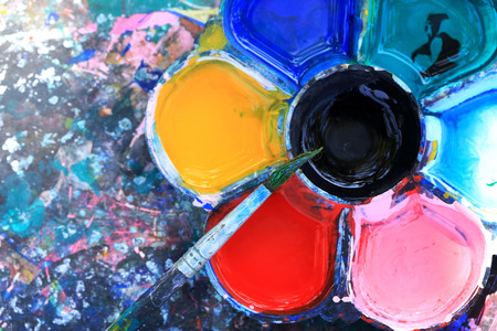 Brushes and dirty watercolor palette on dirty table.