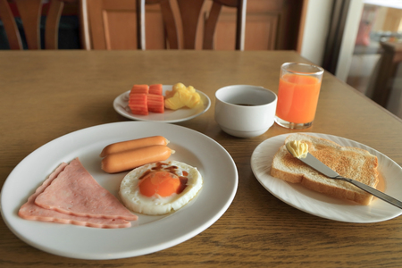 Set of american breakfast on table, fried egg, ham, and sausage, toast and butter, fresh fruits, orange juice and black coffee.の写真素材