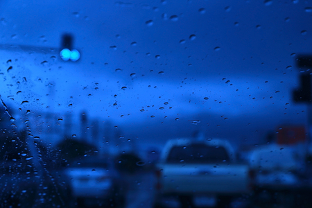 Abstract blurred scene of Road view through car window with rain drops, blue toned color, evening overcast atmosphere.の写真素材