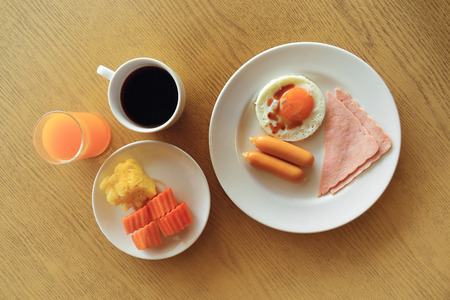 Set of american breakfast on table, fried egg, ham, and sausage with fresh fruits, black coffee, orange juice.の写真素材