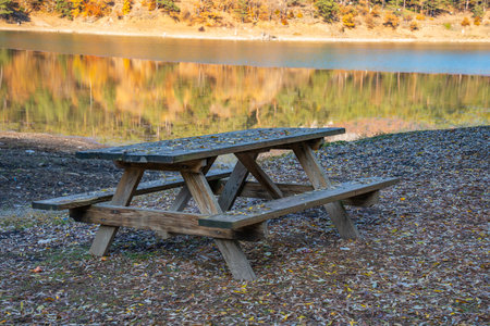 Picnic table with benches by lake in autumn. Rustic wooden outdoor picnic table with mountain lake...