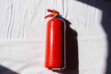 Red fire extinguisher on white fabric surface with shadow. Safety equipment and emergency...