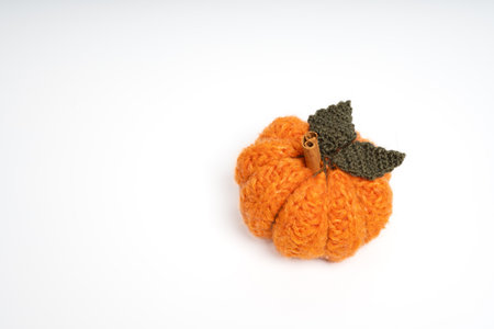 Hand knitted orange pumpkin with green leaf and stem on isolated white background. Knitted orange pumpkin decoration. Craftsmanship and handmade concept. Copy spaceの写真素材