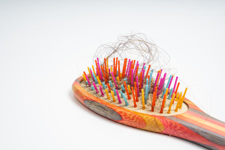 Colorful hairbrush with loose hair strands tangled in bristles on isolated white background. Close up of wooden brush filled with shedding. Grooming, care, maintenance and problemの写真素材