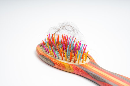 Colorful hairbrush with loose hair strands tangled in bristles on isolated white background. Close up of wooden brush filled with shedding. Grooming, care, maintenance and problemの写真素材