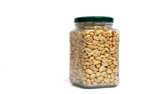 Glass jar with green lid filled with peanuts on isolated white background. Close up of snack peanut filled jar. Nutrition, storage, health and vegetarian concept. Copy spaceの写真素材