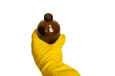 Hand in yellow glove holding brown glass bottle on isolated white background. Close up view. Safety, hygiene, chemistry and care conceptの写真素材