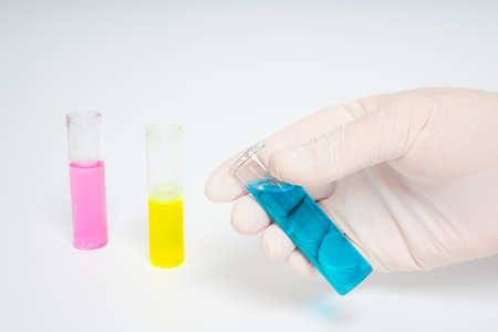 Gloved hands holding glass test tubes with blue, pink and yellow liquids on isolated white...
