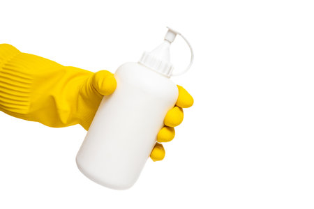 Yellow gloved hand holding white bottle on isolated white background. Bottle held by yellow glove....