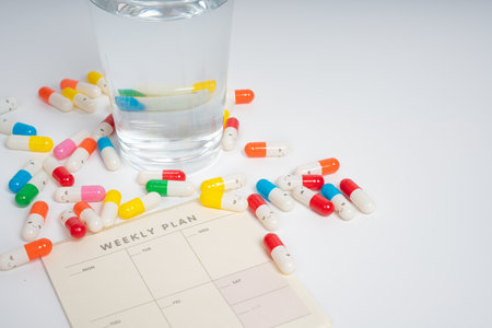 Colorful pills and water glass on weekly plan schedule sheet isolated white background. Medicine...