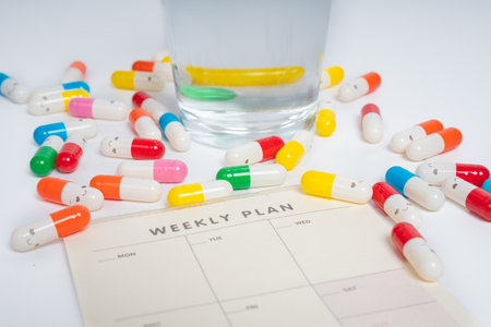 Colorful pills and water glass on weekly plan schedule sheet isolated white background. Medicine...