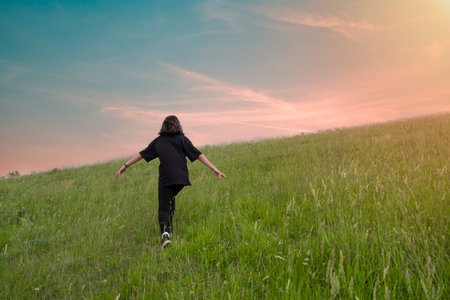 Girl walking on green meadow at sunset. Beautiful summer landscapeの写真素材