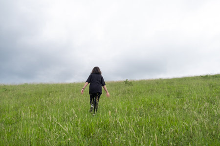 Girl walking on green grass, girl in a black clothes is walking in the meadow and nature, enjoying the freedom, sunny summer dayの写真素材