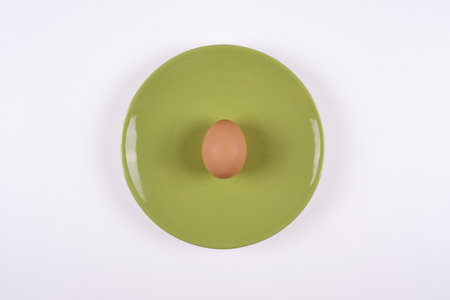 Egg on plate, top view of raw egg on green plate on white background