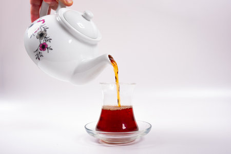 Ceramic teapot pouring hot black tea into cup isolated on white background