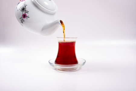Ceramic teapot pouring hot black tea into cup isolated on white backgroundの写真素材