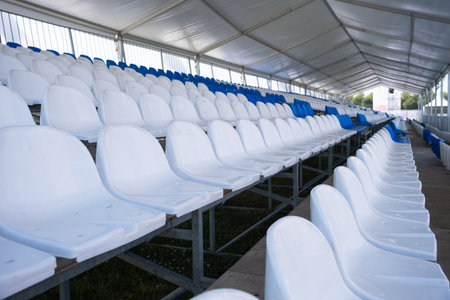 Empty white seats of tribune on sport stadium. Many empty plastic seats in rows in an outdoor...