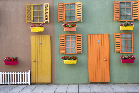Hanging green wooden door and orange and green window with open shutters on colorful and plaster facade, with colorful flower pots in front of themの写真素材