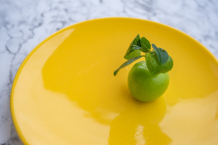 Fresh ripe green fruit on yellow plate with branch on marble background surfaceの写真素材