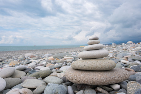 Zen stone balance on beach. Stacked pebbles on rocky beach. Zen stone tower balance on shore. Calm and serene coastal scene under cloudy skyの写真素材