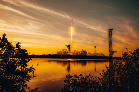 Rocket launch at sunset with fiery trail over water, reflected in golden hues. Exploration, technology and space concept.の写真素材