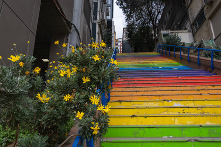 Colorful outdoor staircase with rainbow pattern, surrounded by buildings and greenery. Colorful rainbow stairs with blue railingsの写真素材