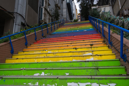 Colorful outdoor staircase with rainbow pattern, surrounded by buildings and greenery. Colorful rainbow stairs with blue railingsの写真素材